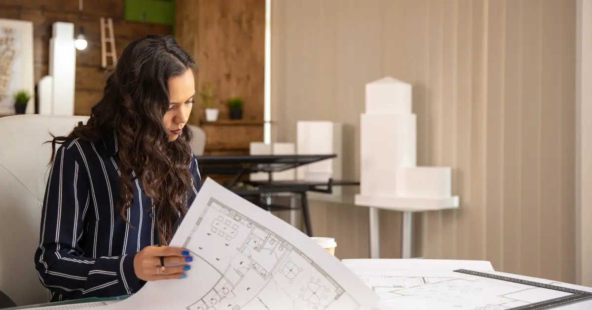 Architect from a Madrid studio reviewing architectural plans at a desk with a model of a building in the background