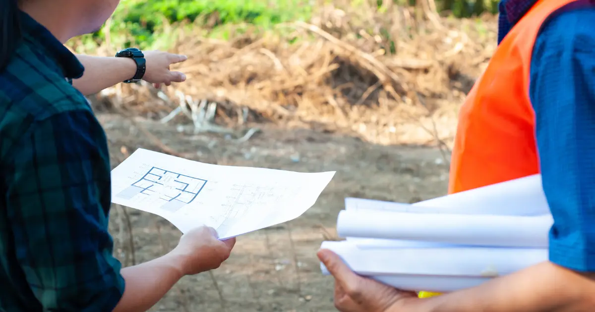 Técnicos revisando planos de vivienda sobre el terreno antes de solicitar los permisos necesarios para construir una casa