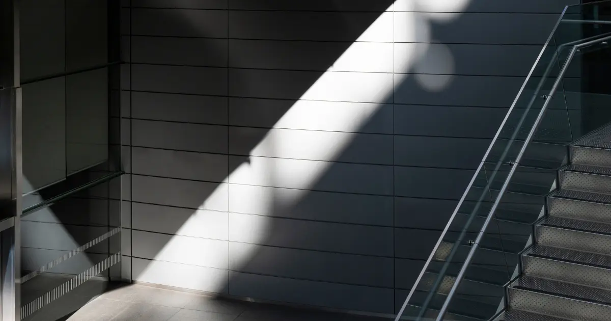 Escalera metálica iluminada por un rayo de luz natural en un edificio en construcción, simbolizando el momento en que se emite la orden de inicio de obra.