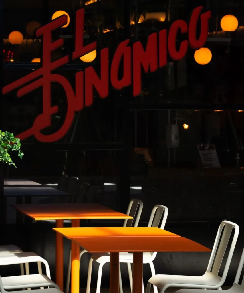 Interior de restaurante moderno con mesas de madera, sillas metálicas y rotulación en cristal