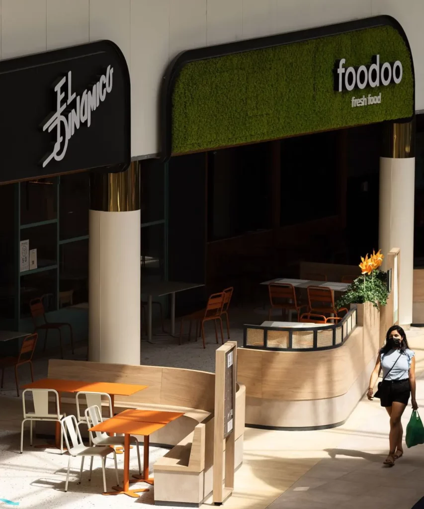 Locales de restauración en centro comercial con diseño moderno, mobiliario exterior y fachada vegetal decorativa