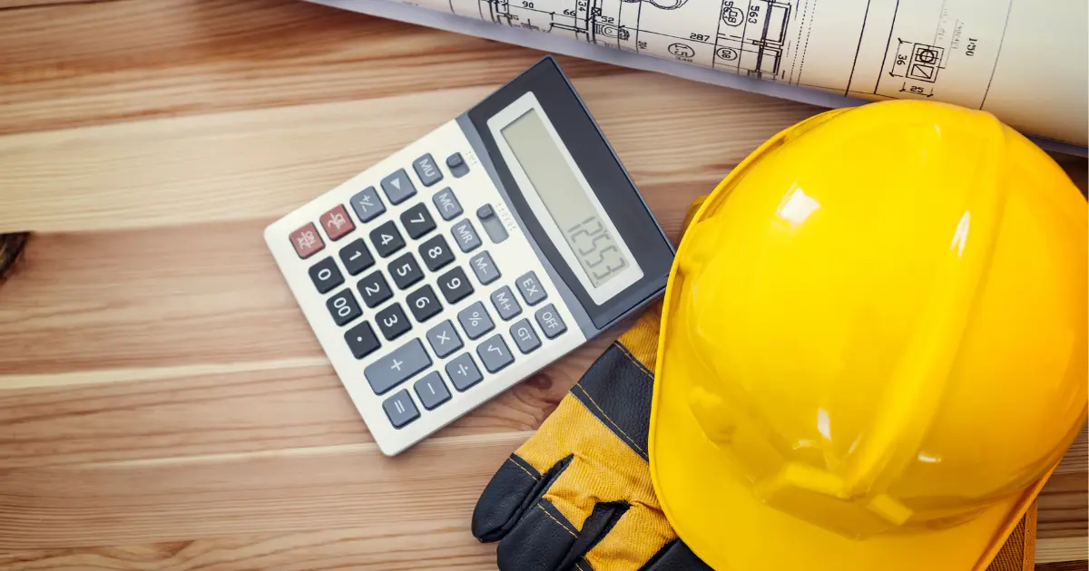 Yellow hard hat with calculator and construction plans on wooden table