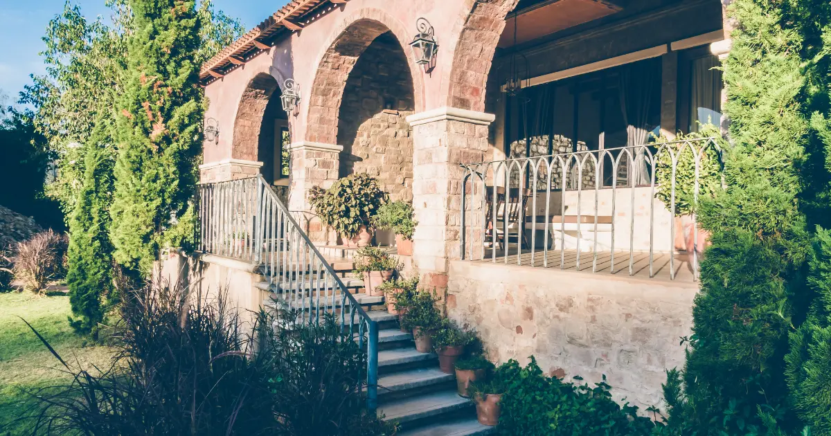 Casa rústica de piedra con porche de arcos, escaleras y jardín