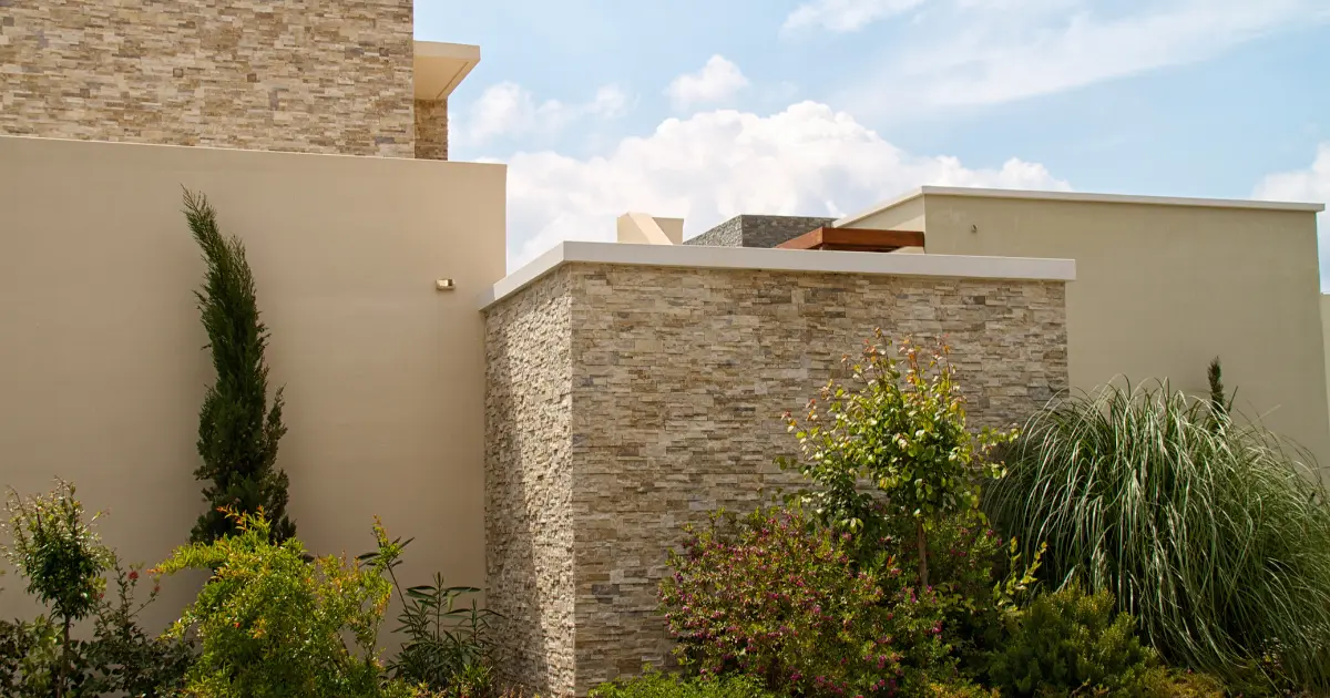 Perimeter wall of a modern villa with stone cladding that delimits the plot of a single-family home with a garden.