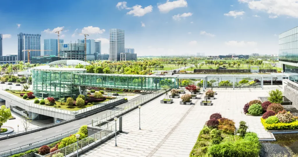 A modern urban space with a glass-enclosed walkway, green spaces, and contemporary architecture