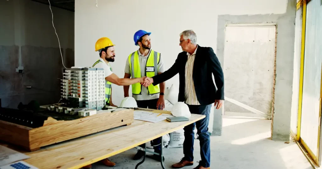 Equipo de construcción y cliente estrechando manos en obra durante desarrollo de proyecto