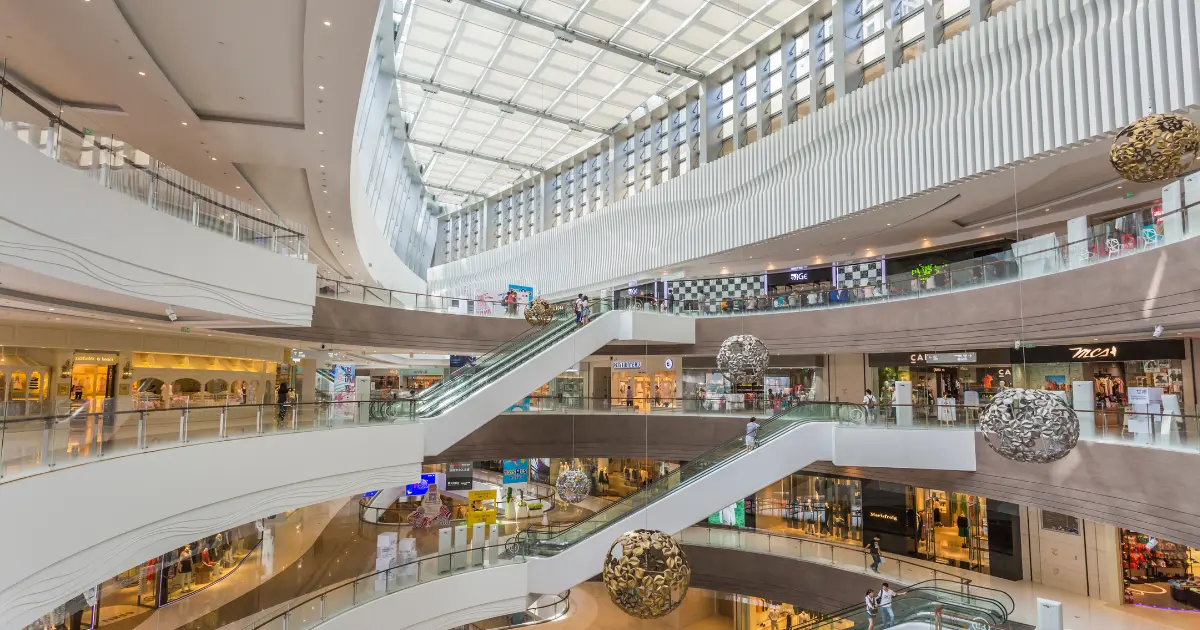 Interior of a multi-level shopping mall with escalators and a large glass roof
