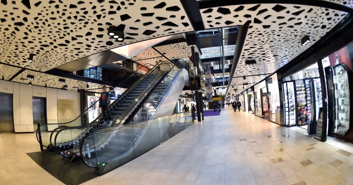 Interior de centro comercial con escaleras mecánicas, tiendas y techo decorativo de diseño contemporáneo