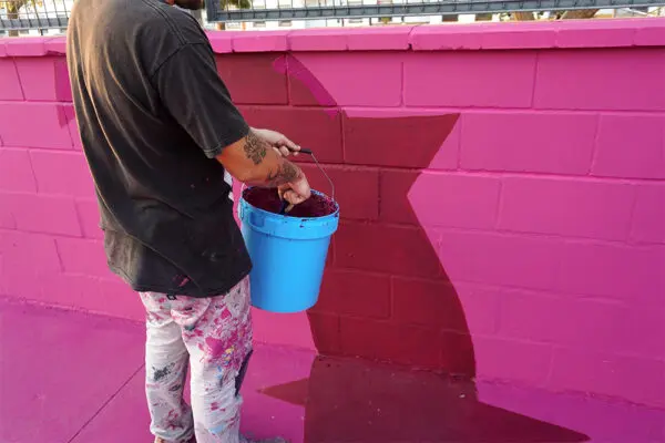 Person painting a pink wall with a blue bucket