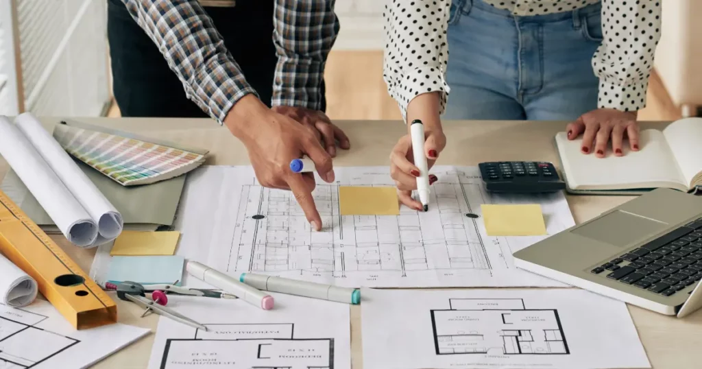Team working on blueprints using design tools, a calculator, and material selection