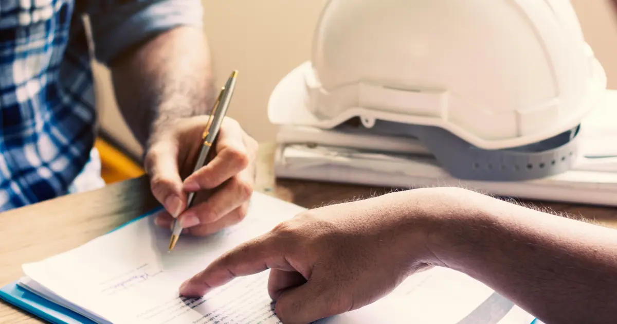 Hands of workers reviewing and pointing at a document next to a safety helmet